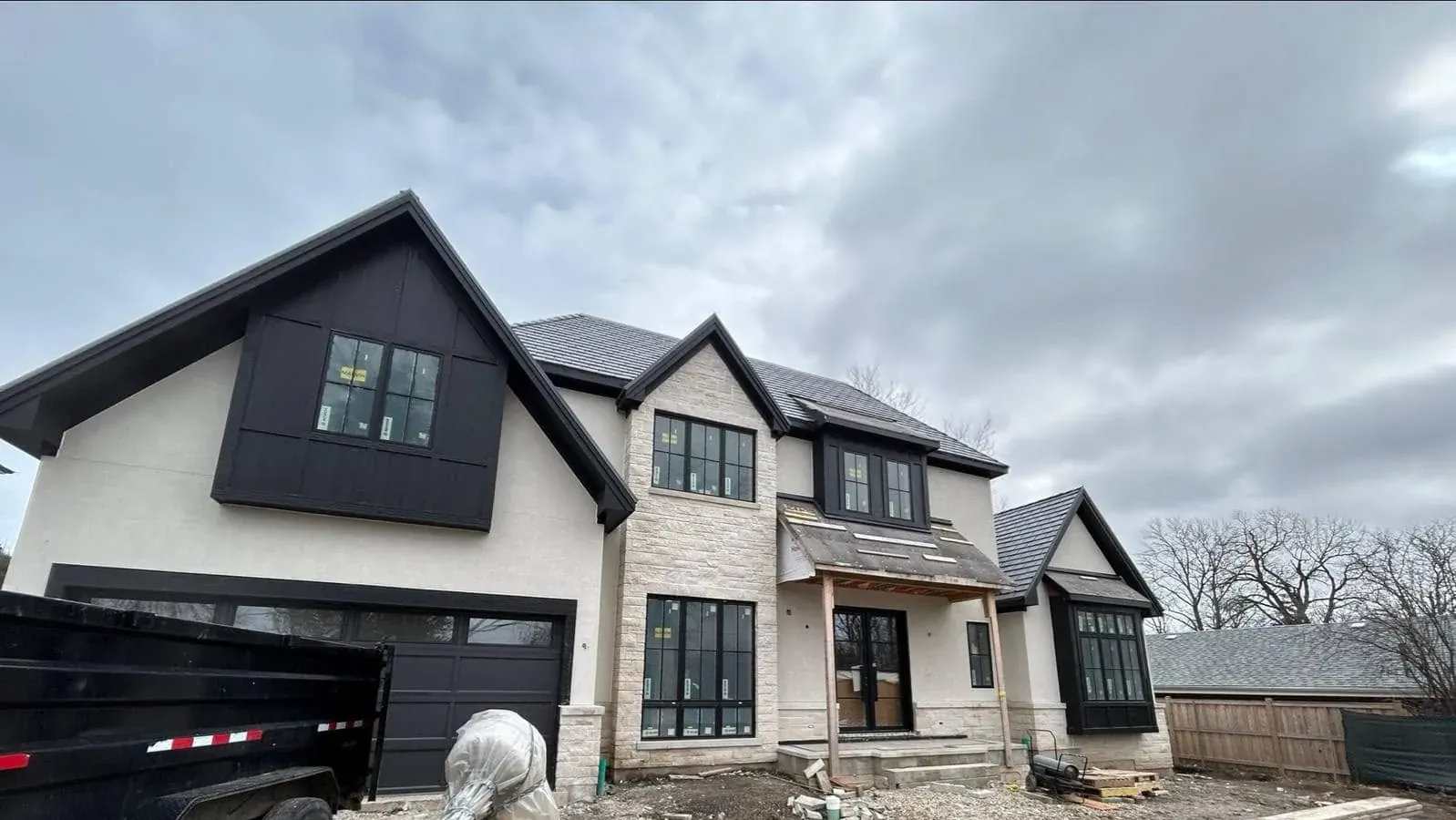 Custom home front elevation with its stucco and stone exterior finished — cream stucco upper walls, a dark board-and-batten gable, light stone veneer and black-framed windows